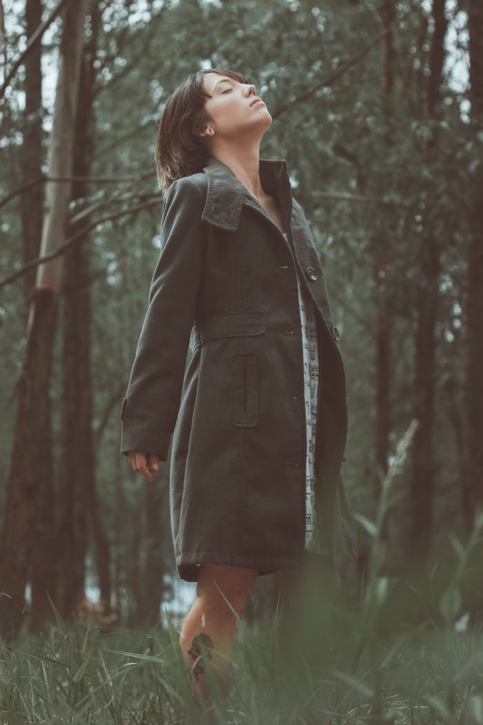A woman standing in a forest with eyes closed, embracing nature's serenity.